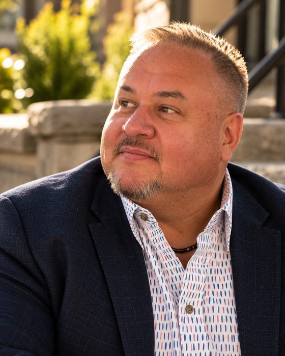 Brian Cardinal seated on stone steps outdoors in a navy blazer, looking off to the side