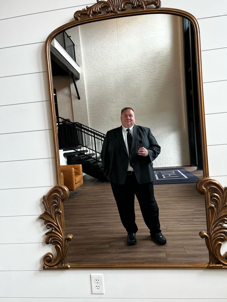 Brian Cardinal standing in a suit, reflected in a gold framed mirror